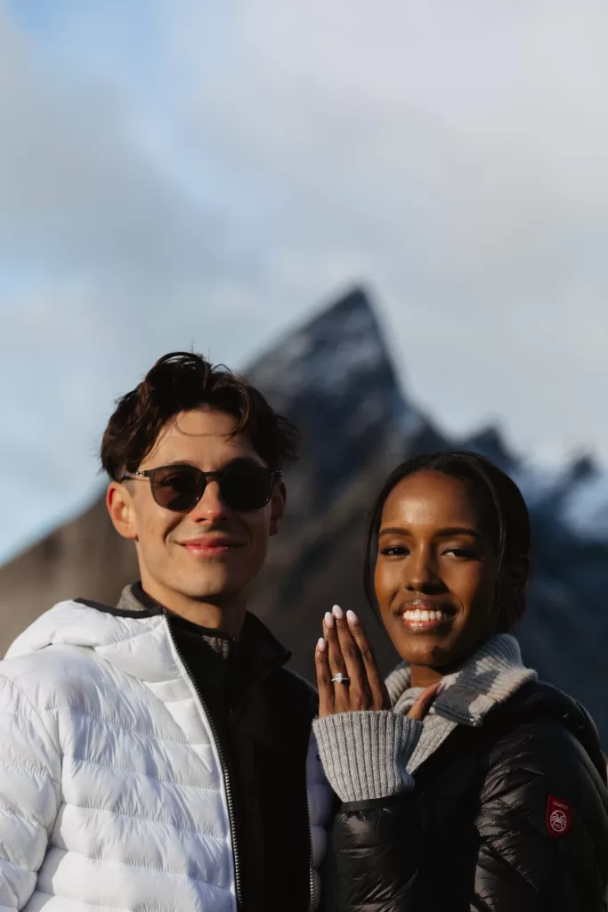 Smiling couple showing engagement ring after proposal in Norway. | 情侣在挪威求婚后展示订婚戒指，满脸笑容。| Lächelndes Paar zeigt Verlobungsring nach dem Antrag in Norwegen. | คู่รักยิ้มแย้มแสดงแหวนหมั้นหลังการขอแต่งงานใน