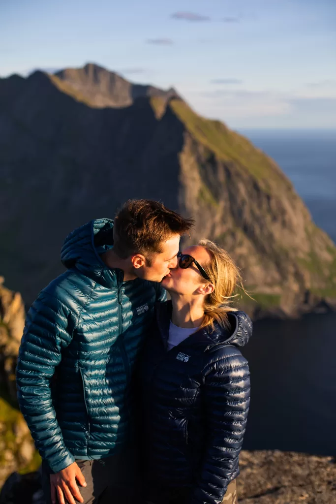 Adventure couple kissing on a Lofoten mountain peak during golden hour – engagement photo in nature.