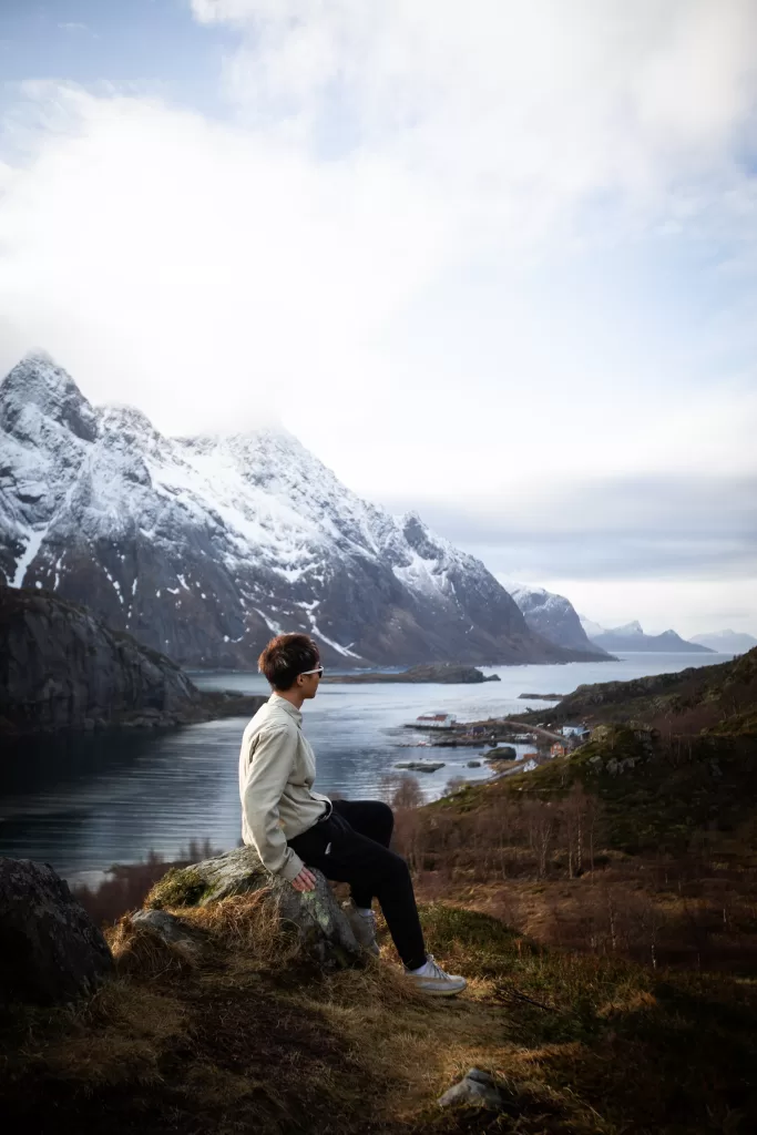 Photography taken in Lofoten - man standing on the top with background of fjords and snow covered mountains