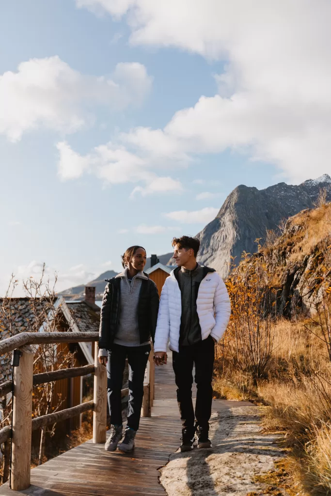 Couple walking hand-in-hand along a scenic wooden path in Lofoten – cozy autumn vibes in Norway.