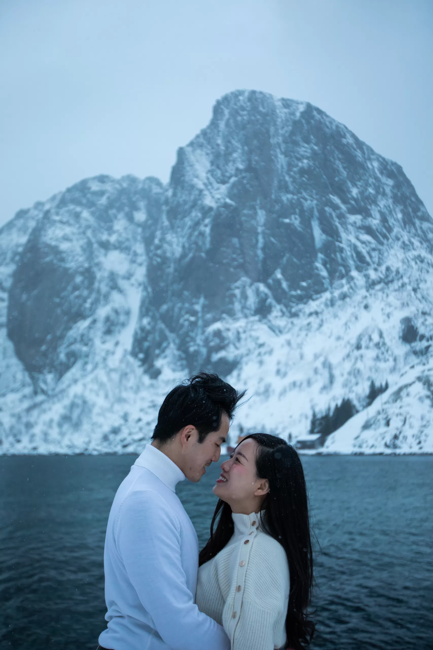 Couple looking into each other's eyes in front of a towering Lofoten peak – winter engagement photo.