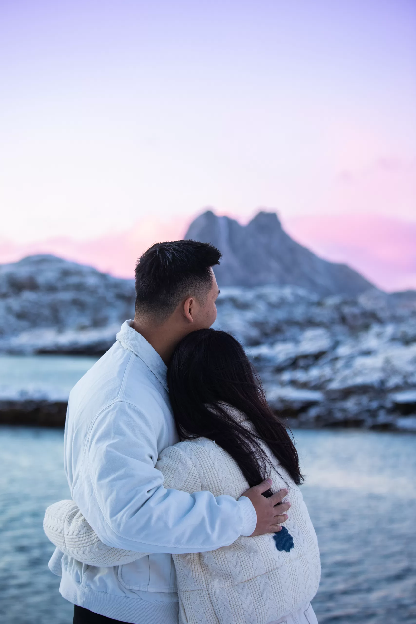 Romantic couple embracing by the Arctic sea in Lofoten during a pastel sunrise.
