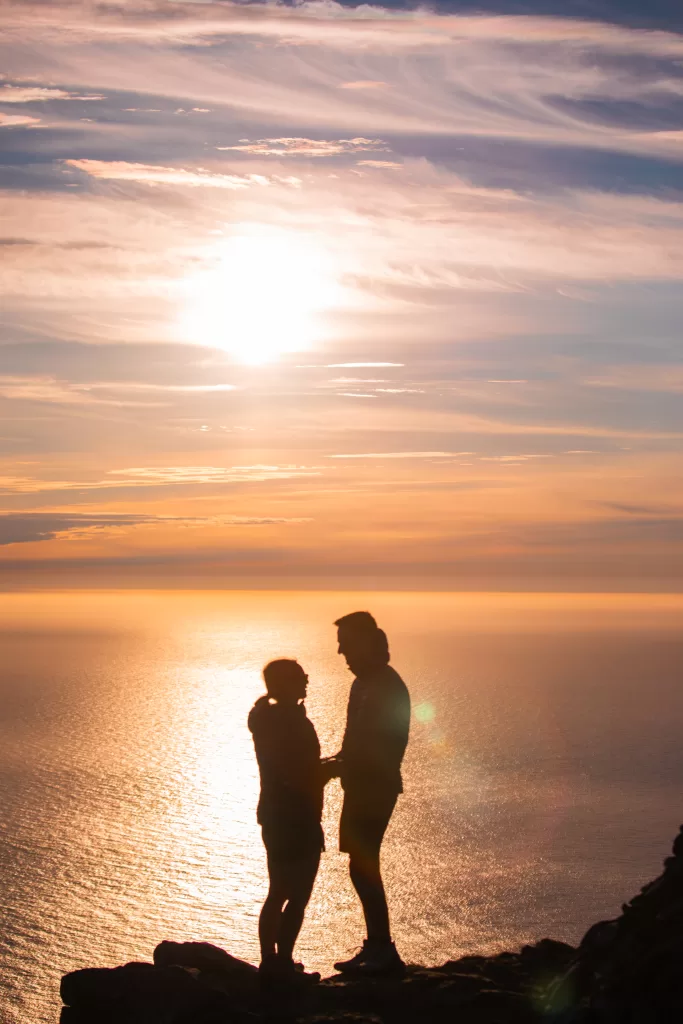 Silhouetted couple holding hands at sunset over the ocean, captured in the dramatic mountains of Lofoten.